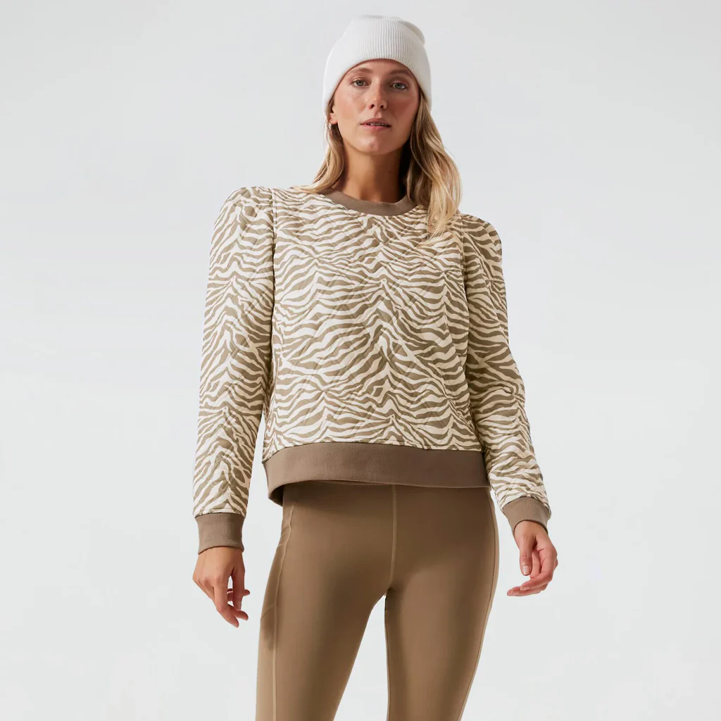 Model in classic beige-and-white zebra-stripe sweatshirt with puffed shoulders, taupe leggings, and a white beanie for an effortless, fun, high-end look.
